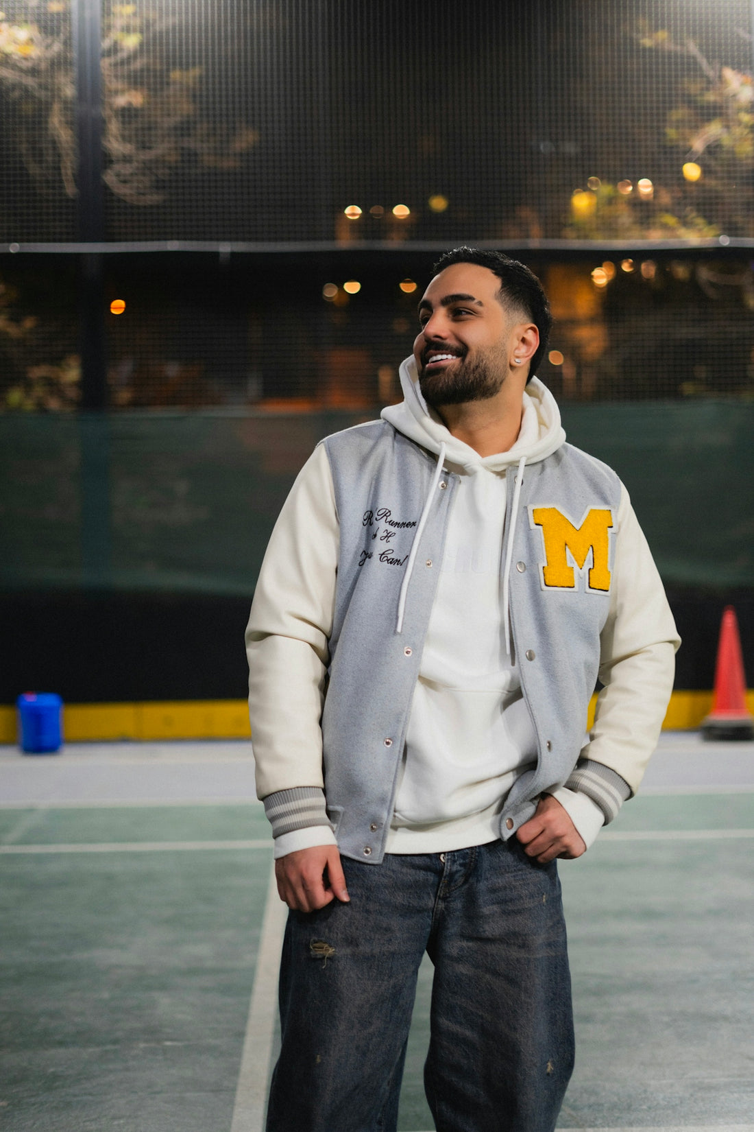 Man in varsity jacket and hoodie smiles outdoors