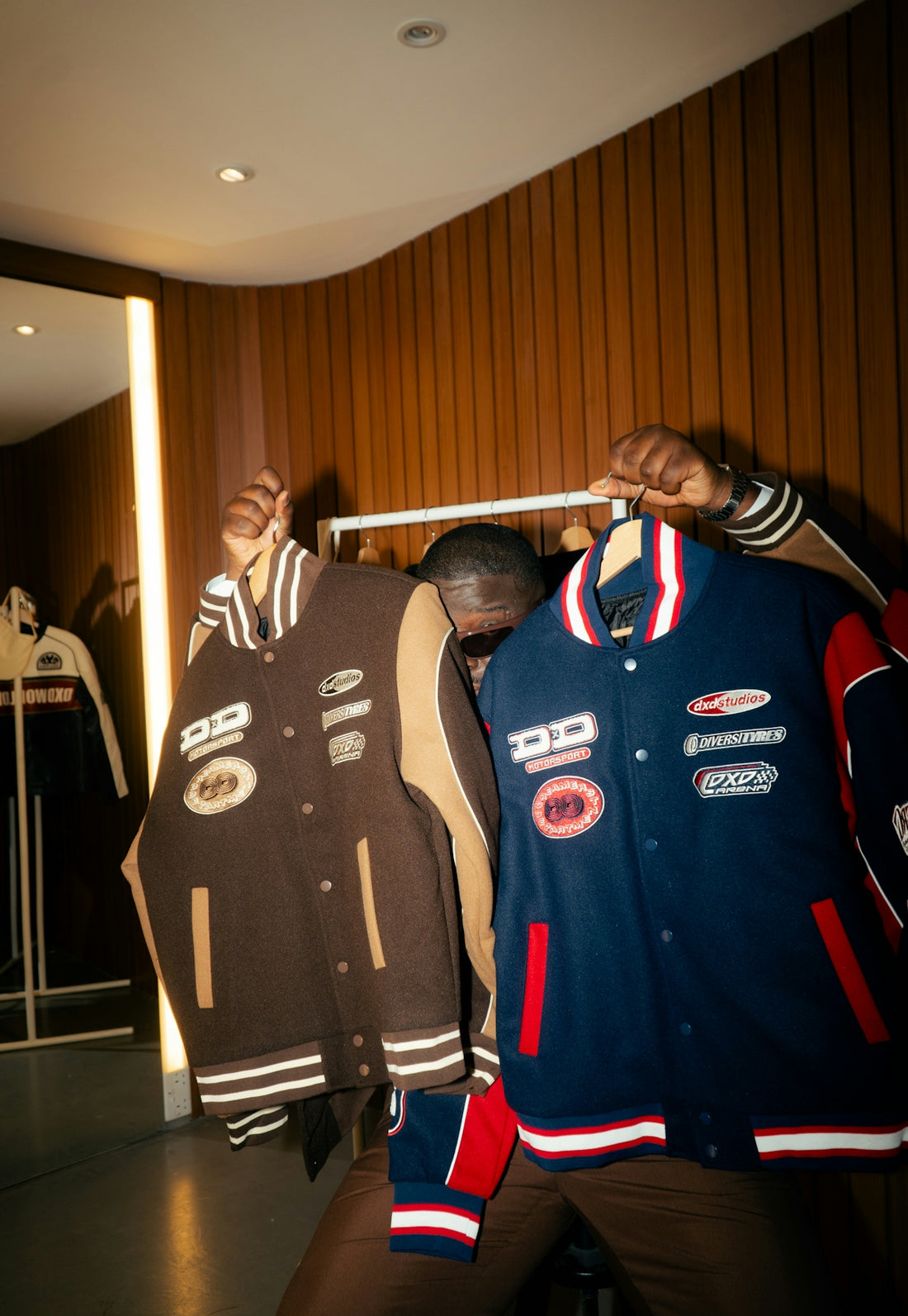 Man holds two varsity jackets, brown and blue.
