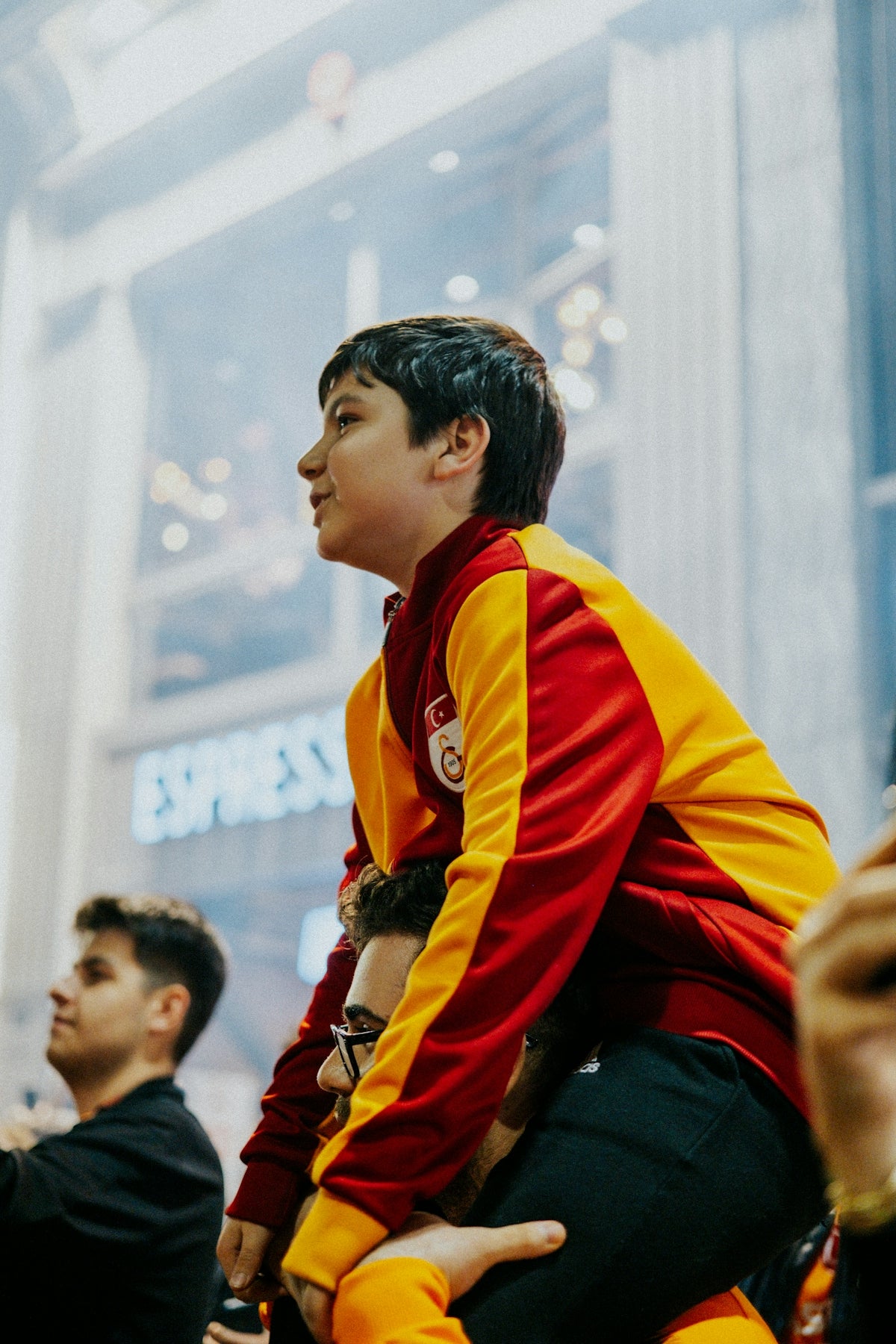 Boy on man's shoulders wearing red and yellow sports jacket